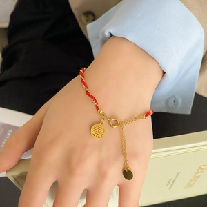 Detailed view of red braided bracelet with golden beads and hollow Xi character charm