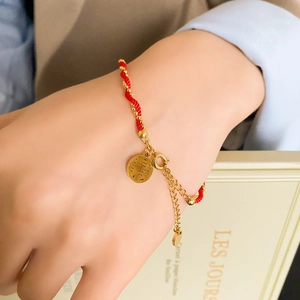 Detailed macro of red braided rope bracelet with golden beads and a Xi character pendant