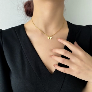 Gros plan d'un collier pendentif papillon doré porté par un mannequin sur un col en V noir