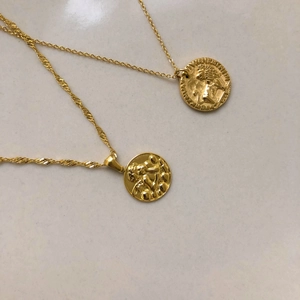 Dettaglio di ciondoli a moneta con leone e figure in oro goffrato su catenine sottili