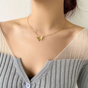 Close-up of gold hollow butterfly pendant necklace worn by a model on grey knitwear