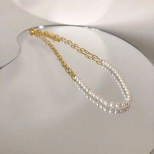 Elegant gold chain necklace with half white pearls displayed on a reflective mirror