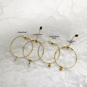 Flat lay of four minimalist gold-plated bangles with pearl and bead charms on white background