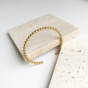 Minimalist gold-plated bead open cuff bracelet displayed on natural stone travertine base