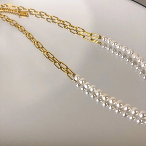 Macro detail of gold metal chain links and white pearl necklace on a reflective surface