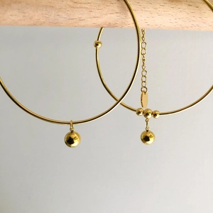 Macro view of polished gold hoop earrings with metallic beads on wooden stand