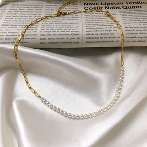 Elegant gold paperclip chain and white pearl necklace on white satin background