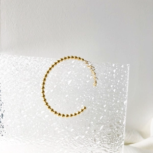 Minimalist gold beaded open bangle bracelet displayed on a geometric acrylic stand