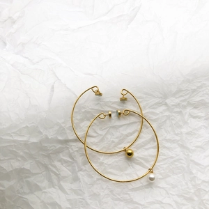 Detail of two-piece gold open bracelets featuring elegant pearl and metal ball charms