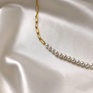 Detailed view of gold paperclip chain and white pearl necklace on white silk fabric