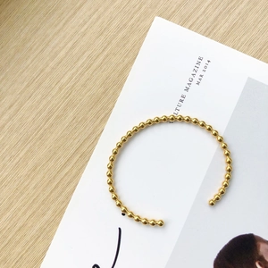 Detailed view of a minimalist rose gold beaded cuff bracelet on a white magazine background