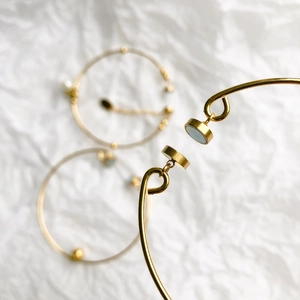 Detail of gold-plated bracelets featuring elegant pearls and blue gemstones in close-up shot