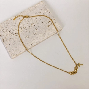 Collier à croix plaqué or minimaliste avec maillons épais sur fond de pierre beige