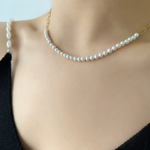 Detailed close-up of a pearl necklace with golden paperclip chain on a model's collarbone