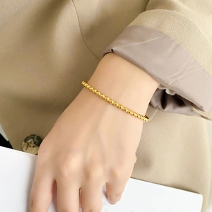 Close-up of minimalist gold beaded bracelet showing metallic luster on a model's wrist