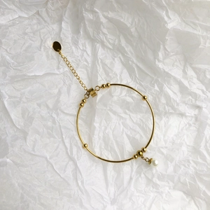 Detail of gold pearl bangle with adjustable chain and round brand tag on white paper