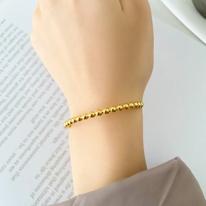 Close-up of minimalist gold-plated beaded bangle showing polished metallic texture