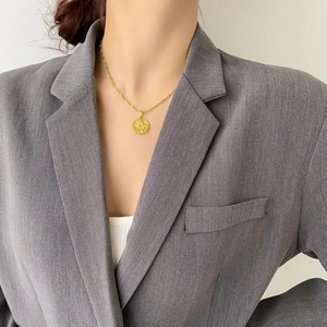 Dettaglio della collana con ciondolo a moneta d'angelo dorata su blazer grigio