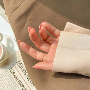 Close-up of two slim gold frosted rings worn by a model in a warm aesthetic scene