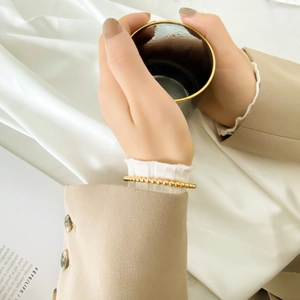 Polished rose gold beaded bracelet styled with a chic khaki suit and white lace sleeve