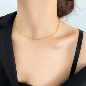 Collana minimalista a sfere placcata in oro indossata da modella su blazer nero