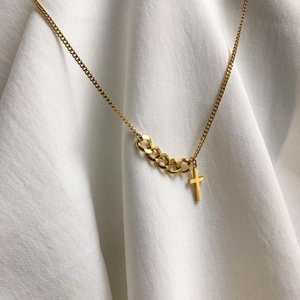 Détail du pendentif croix dorée avec chaîne mixte posé sur un tissu blanc fluide