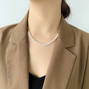 Close-up of elegant pearl necklace with gold chain link texture on a model wearing a blazer