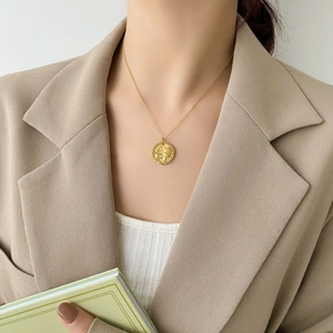 Primo piano di una collana con ciondolo a moneta d'oro con rilievo su un blazer beige