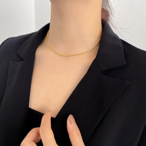 Primo piano della collana minimalista con perline dorate indossata sopra un blazer nero
