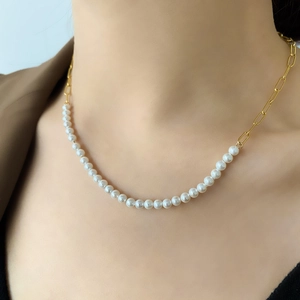 Close-up of pearl and gold paperclip chain necklace on neck with minimalist suit