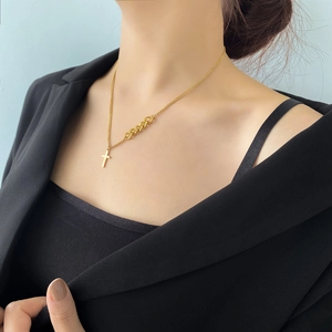 Détail d'un collier croix doré avec chaîne asymétrique porté par un mannequin