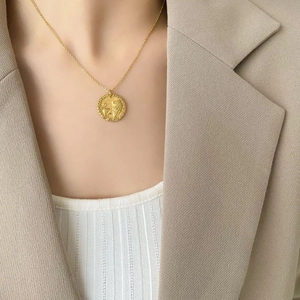 Dettaglio di una collana vintage con ciondolo a moneta di leone d'oro su un top bianco