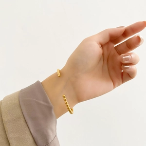Detail of a gold-plated open bangle with bead texture on a model's wrist with beige suit