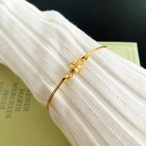 Detail of minimalist gold-tone bracelet with cylindrical magnetic clasp on pleated fabric