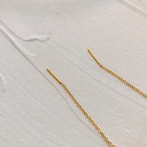 Detailed close-up of golden tassel ear threads on a textured minimalist background