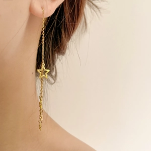 Close-up of a gold star tassel drop earring on a model with long metal chains