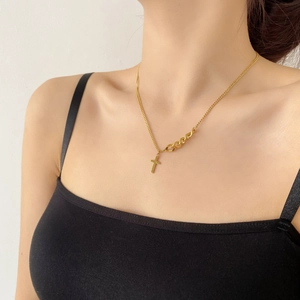 Gros plan d'un collier croix doré avec chaîne asymétrique porté par un mannequin