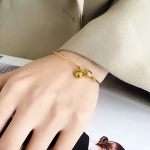 Minimalist gold open cuff bracelet with small bell and cylinder charms on a model's wrist