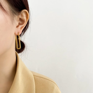 Dettaglio di orecchini a forma di U ritorti in oro su modella con blazer giallo