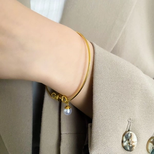 Close-up of a minimalist gold bracelet with a round pearl and ring pendant on a wrist