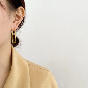 Dettaglio degli orecchini a U dorati a maglia intrecciata indossati da una modella elegante