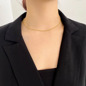 Dettaglio di una collana girocollo minimalista con perline d'oro su un blazer nero