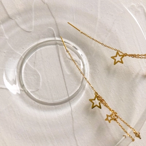 Macro shot of gold tassel star earrings on a glass tray with long chain details