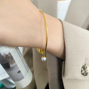 Close-up of minimalist gold open bangle with a white pearl charm on a woman wrist