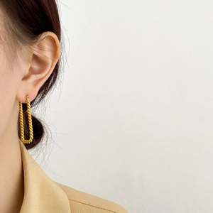 Dettaglio di una modella che indossa un orecchino rettangolare a corda dorato dal design sobrio