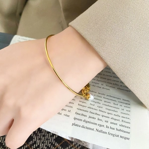 Detailed view of a minimalist gold bangle with a white pearl and bead on a woman's wrist