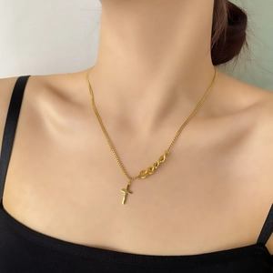 Détail du collier croix dorée avec chaîne asymétrique porté par un mannequin