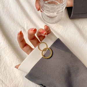 Detailed view of two minimalist gold beaded stackable rings on grey fabric background