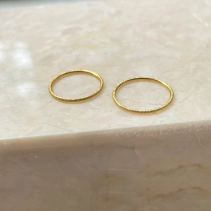 Detail of two golden frosted minimalist rings on a marble surface with starry texture