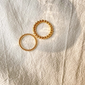 Detail view of two minimalist gold beaded rings on fabric showing smooth texture and luster